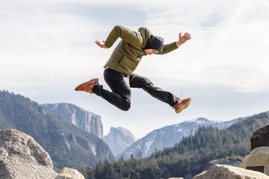 Adventurous man leaps over rocks with mountains and trees in the background.