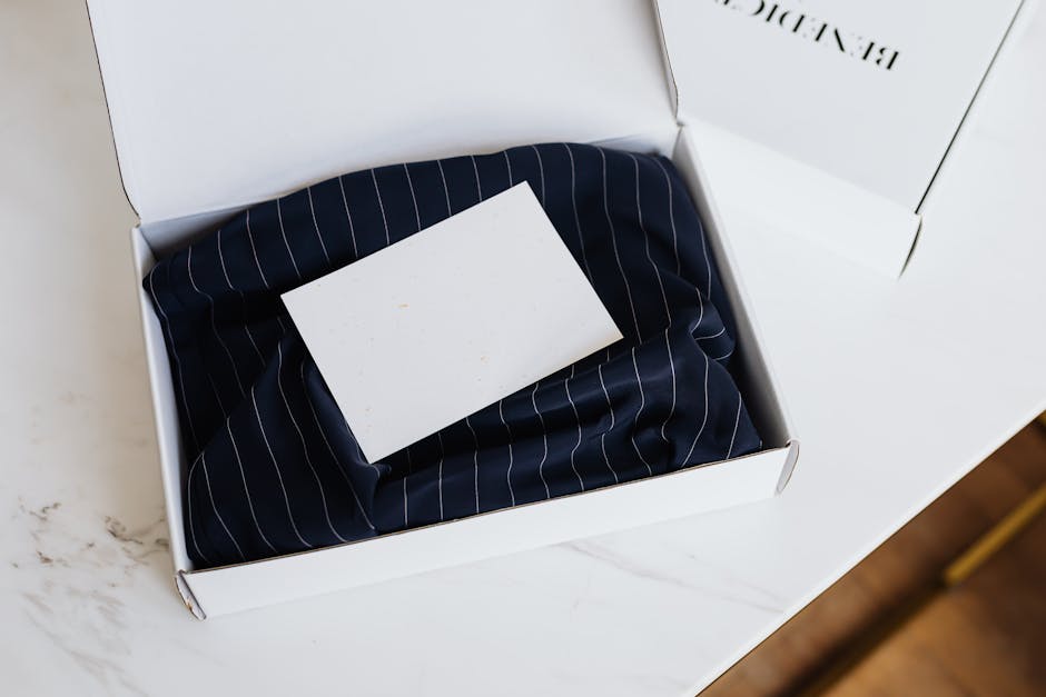 Minimalist white box with clothing and blank card on a marble table, ideal for branding.