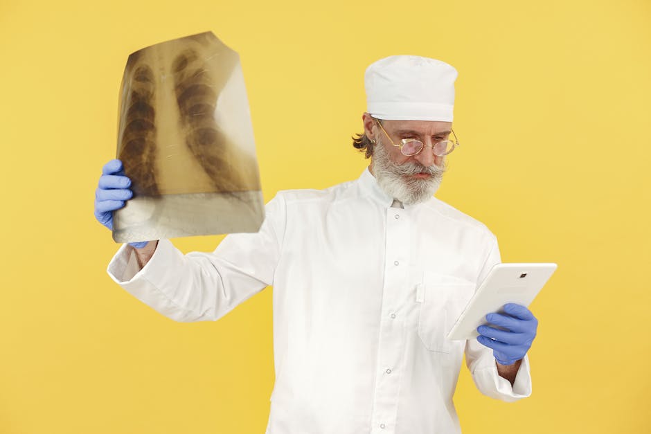 Bearded senior doctor in white coat examining an x-ray while holding a tablet against a yellow background.