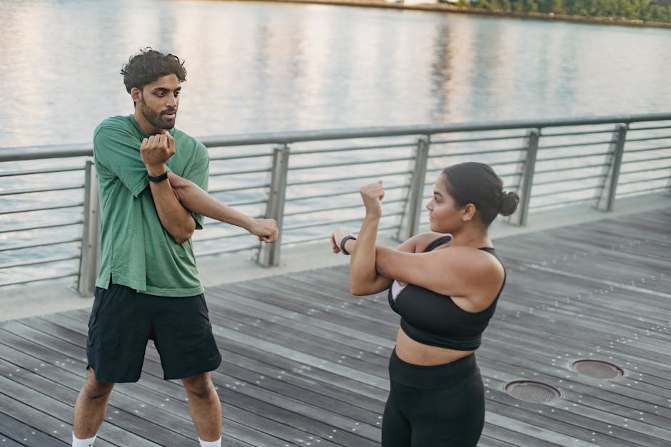 A man and woman stretching together on a boardwalk by the river, promoting fitness and healthy lifestyle.