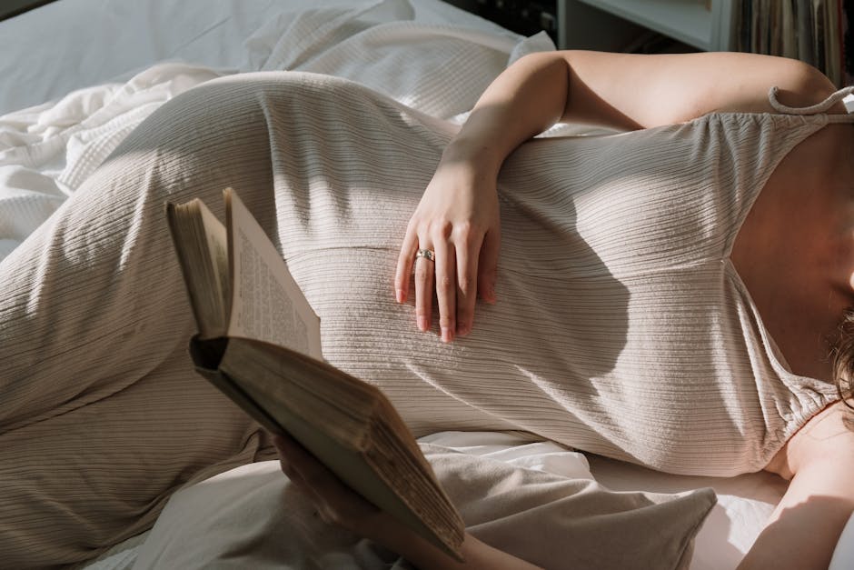 Pregnant woman with flowing dress reading a book in bed, enjoying peaceful leisure time.