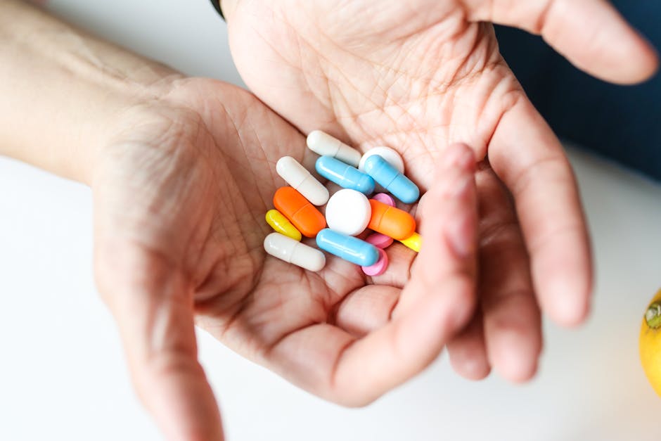 Assorted colorful pills and capsules in hands, representing healthcare treatment.