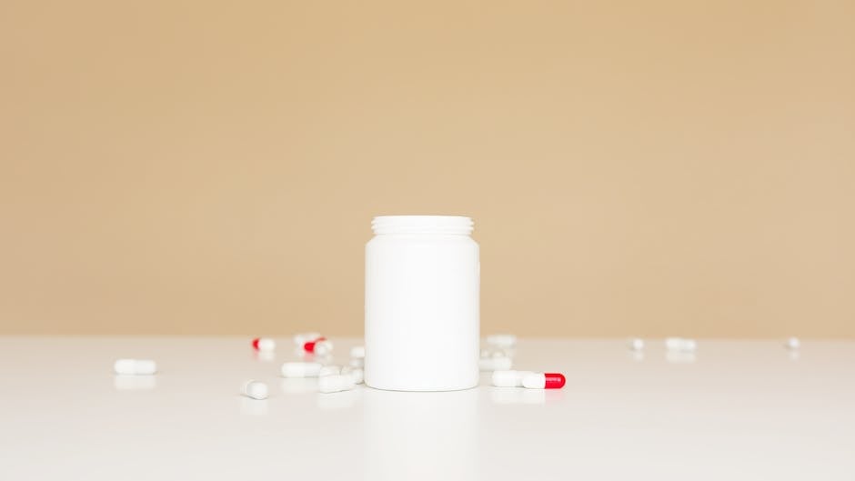 Open white plastic bottle and red and white pills scattered around on white table