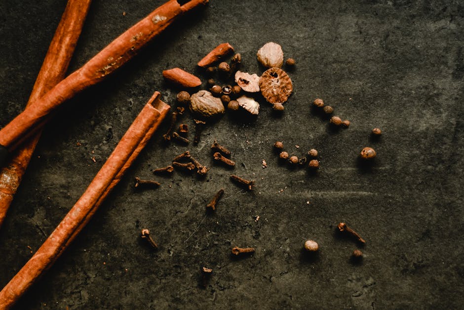A rustic top view of cinnamon sticks and assorted spices on a dark surface.