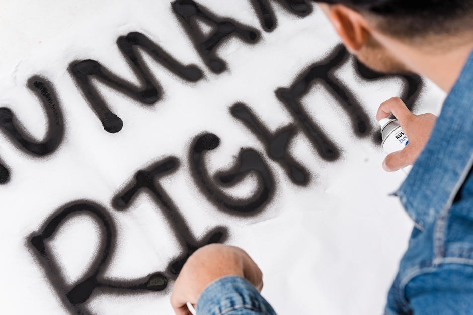 Close-up of a person spray painting the words 'Human Rights' on a wall.