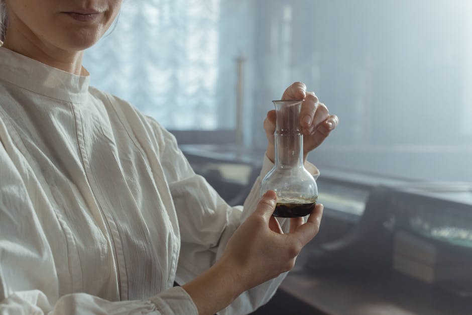 A woman in a white shirt delicately holds a glass flask in a softly lit laboratory.