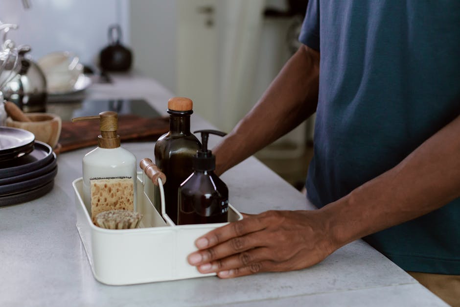 A close-up of a man organizing cleaning products in a modern kitchen environment.