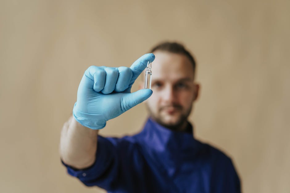 A male healthcare worker in protective gloves holding a small vial, focusing on medical research and safety.