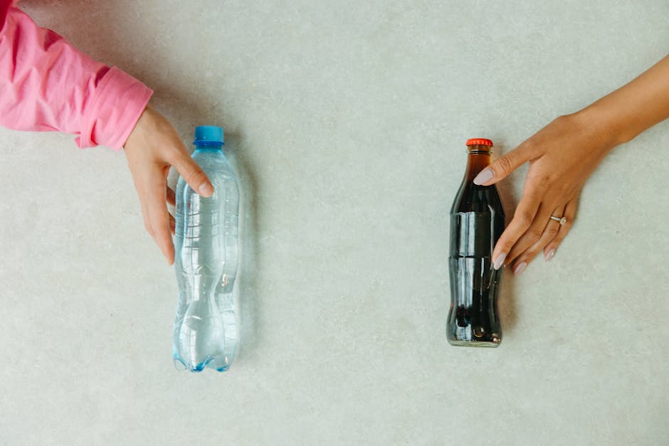 Close-up of hands reaching for a bottled water and a soda bottle on a light surface.