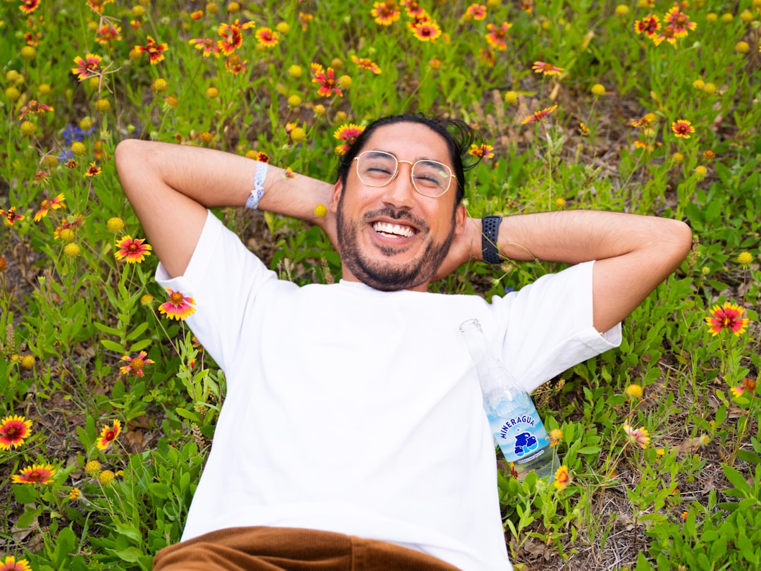 a man laying in a field of flowers with a bottle of water