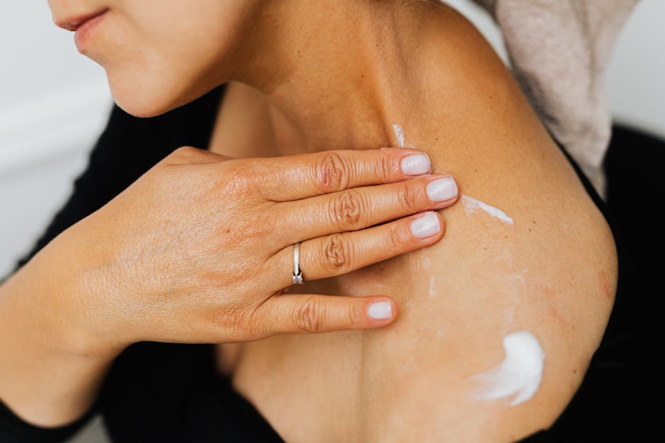 A close-up image of a woman applying skincare lotion on her neck with manicured hands.