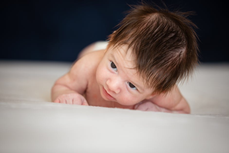 Charming newborn baby boy lying on a soft white blanket, showcasing innocence and cuteness.