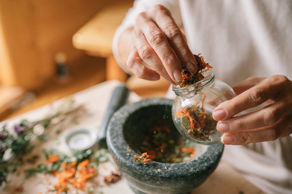 Close-up of hands using a stone mortar to grind herbs and petals for a natural remedy.