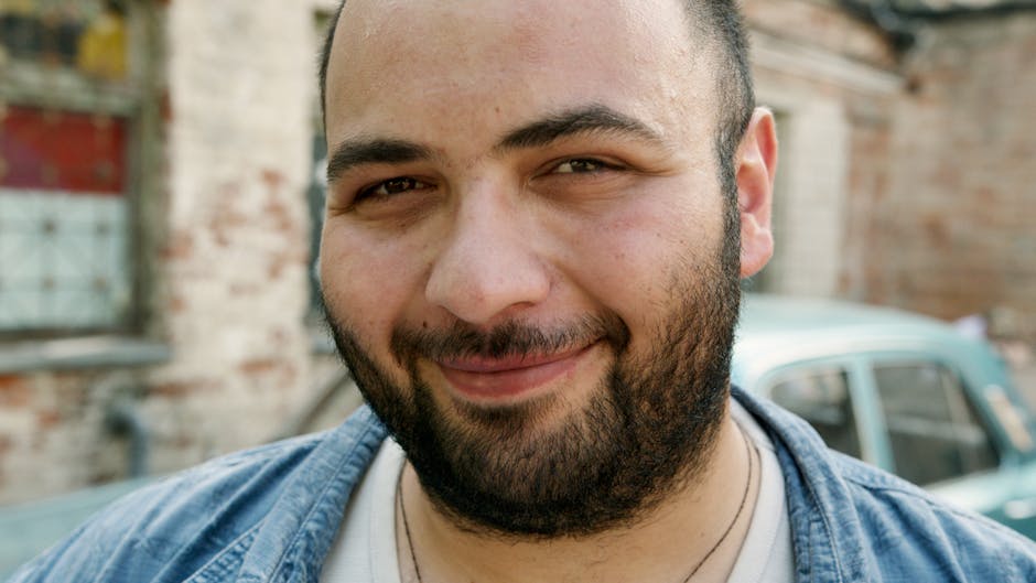 Close-up portrait of a smiling man with a beard outdoors.