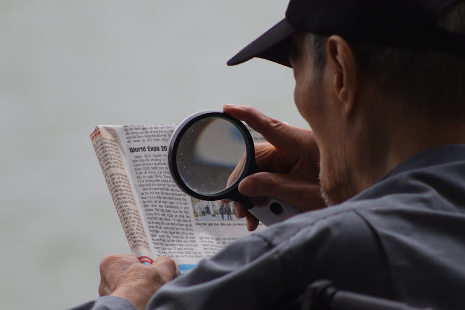 Elderly man using a magnifying glass to enhance text in a newspaper.