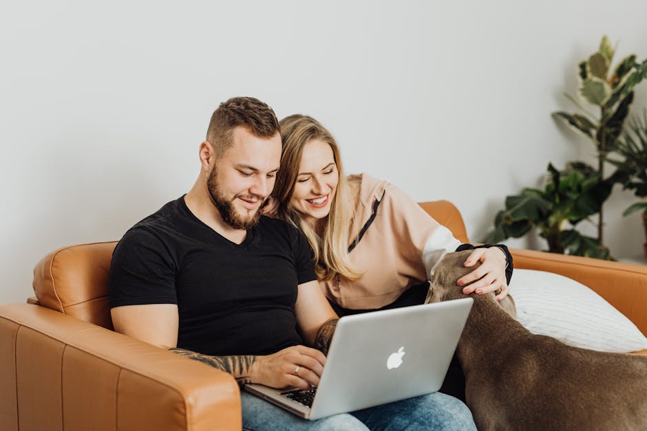 A joyful couple sitting on a sofa with a laptop and their dog, enjoying leisure time indoors.