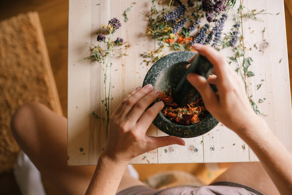 Top view of hands using a mortar and pestle to grind herbs on a wooden surface.