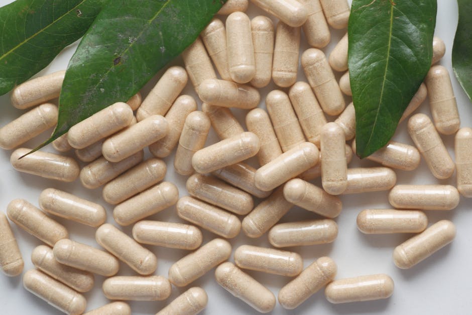 Organic medicine capsules with fresh green leaves on a white background.