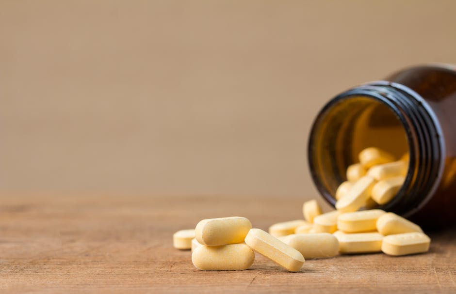 Yellow tablets spilling from an open brown glass bottle on a wooden surface, isolated on beige background.